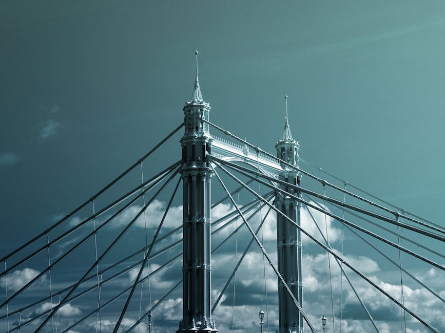 Close-up view of the suspension cables and ornate towers of Hammersmith Bridge against a partly cloudy sky during daytime, with a focus on the structural details and weathered metal surfaces of the historic bridge, highlighting its architectural features without any cleaning tools or surfaces visible, as would be relevant for discussing maintenance or inspection processes related to surface cleaning or preservation by Hammersmith Carpet Cleaning.